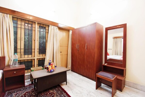 Habitación de hotel con armario de madera, mesita de noche, banco, espejo y ventana con cortinas.