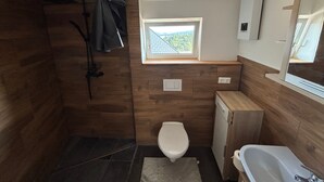 Un baño pequeño con ducha, inodoro y bañera, paredes de madera, una ventana y una luz en el techo.