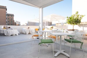 An outdoor patio with white tables and chairs, some with green cushions, and umbrellas. - Azzurra Luxury with Shared Terrace, Wi-Fi and Air Conditioning (Marsala)