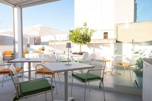 An outdoor patio area with white metal tables and chairs, some with green cushions, and umbrellas providing shade. - Azzurra Luxury with Shared Terrace, Wi-Fi and Air Conditioning (Marsala)