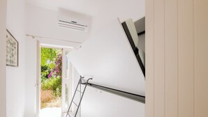 Une pièce avec un mur blanc, une porte donnant sur un jardin et une échelle appuyée contre le mur.