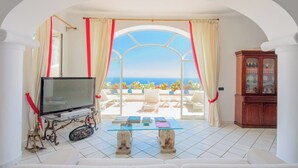 Un salon avec un téléviseur, une table en verre et une vue sur la mer.