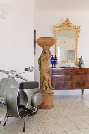 A room with a vintage scooter, a decorative statue, a wooden dresser, and a mirror with an ornate frame. - Villa Cristina | Panoramic ocean view, main level with no steps, Praiano (Praiano)