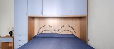Un dormitorio con cama, mesita de noche, lámpara y armario.