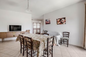 Een eethoek met een tafel, stoelen, een televisie en kunst aan de wand.