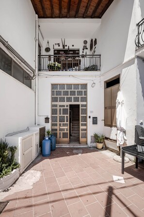 A courtyard with a wooden door, potted plants, a white wall, and a metal railing. - Domus de Sole | Beach 100m Away & Sea-View Terrace (La Caletta)