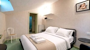 Une chambre d’hôtel avec un lit, une chaise, une petite table et un tableau au mur.
