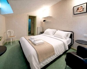 Ein Hotelzimmer mit einem Bett, einem Sessel, einem kleinen Tisch und einem Bild an der Wand.