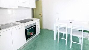 Une cuisine avec des meubles blancs, un évier, un four et une table à manger avec des chaises.
