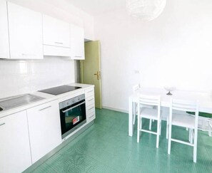 Eine Küche mit weißen Schränken, einem Spülbecken, einem Backofen und einem Esstisch mit Stühlen.