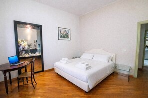 Een hotelkamer met een bed, een bureau met een laptop, een spiegel en een lijst met een foto aan de muur.