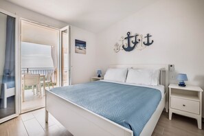 A bedroom with a bed, a nightstand, a wall-mounted anchor decoration, a window with a view, and a door leading to an outdoor area. - Sea View Costa Paradiso | 8 guests (Trinità d'Agultu e Vignola)