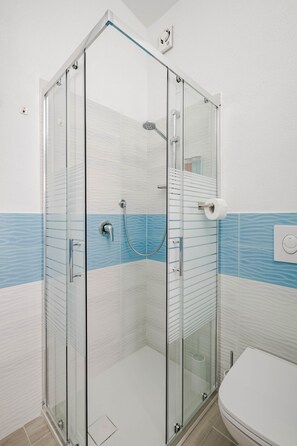 A glass-enclosed shower with a white toilet and a blue-striped wall. - Sea View Costa Paradiso | 8 guests (Trinità d'Agultu e Vignola)