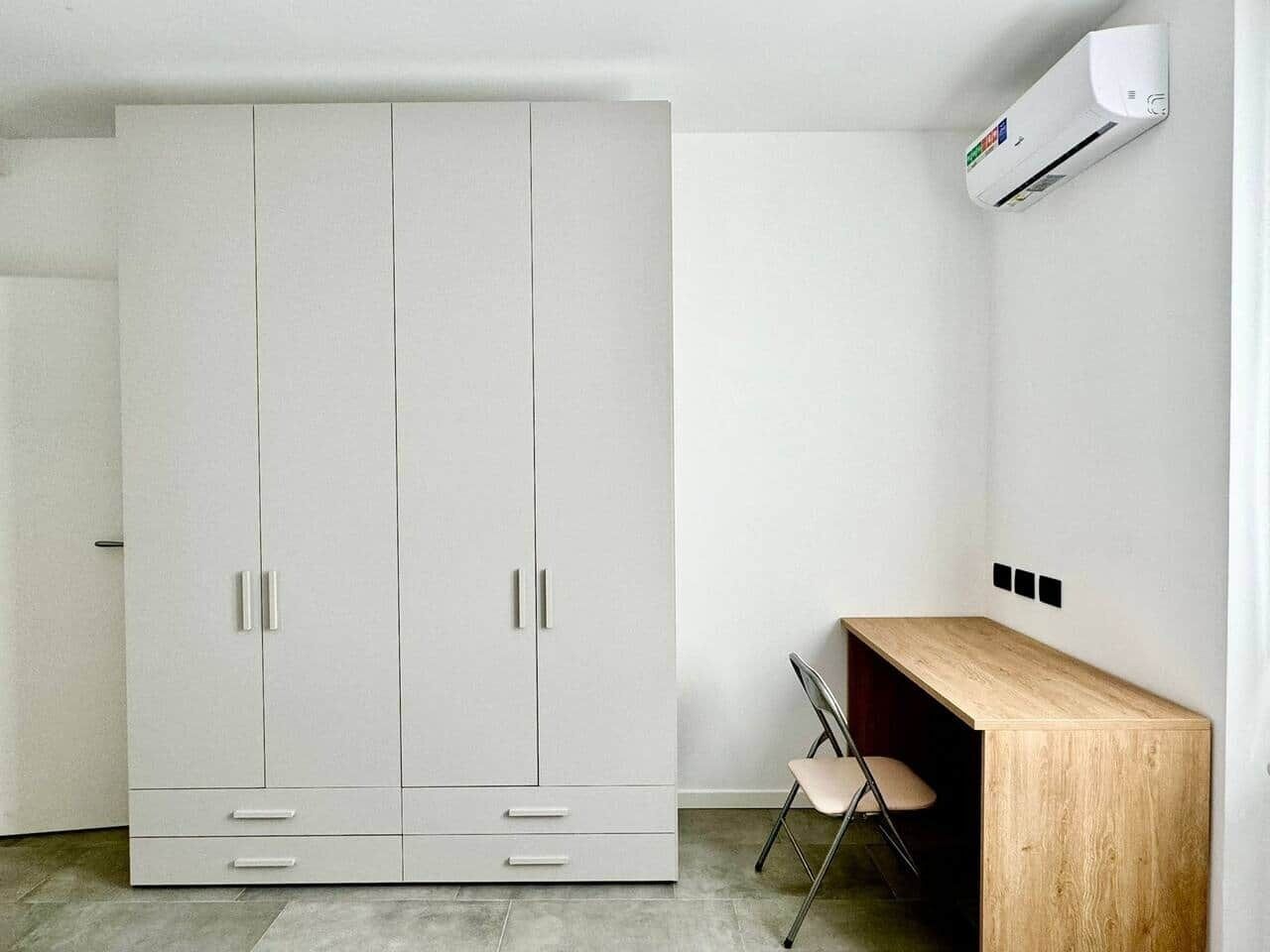 Une pièce comprenant une grande armoire blanche, un bureau en bois, une chaise et un appareil de climatisation fixé au mur.