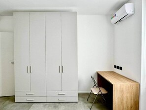 A room with a large white wardrobe, a wooden desk, a chair, and an air conditioning unit on the wall. - Design House | Parking,Terrace (Bergamo)