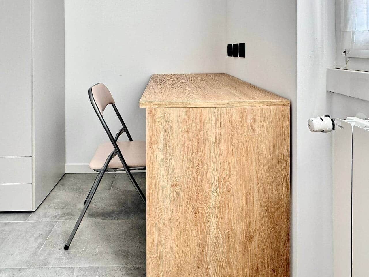 Une pièce avec un bureau en bois, une chaise et un meuble blanc.