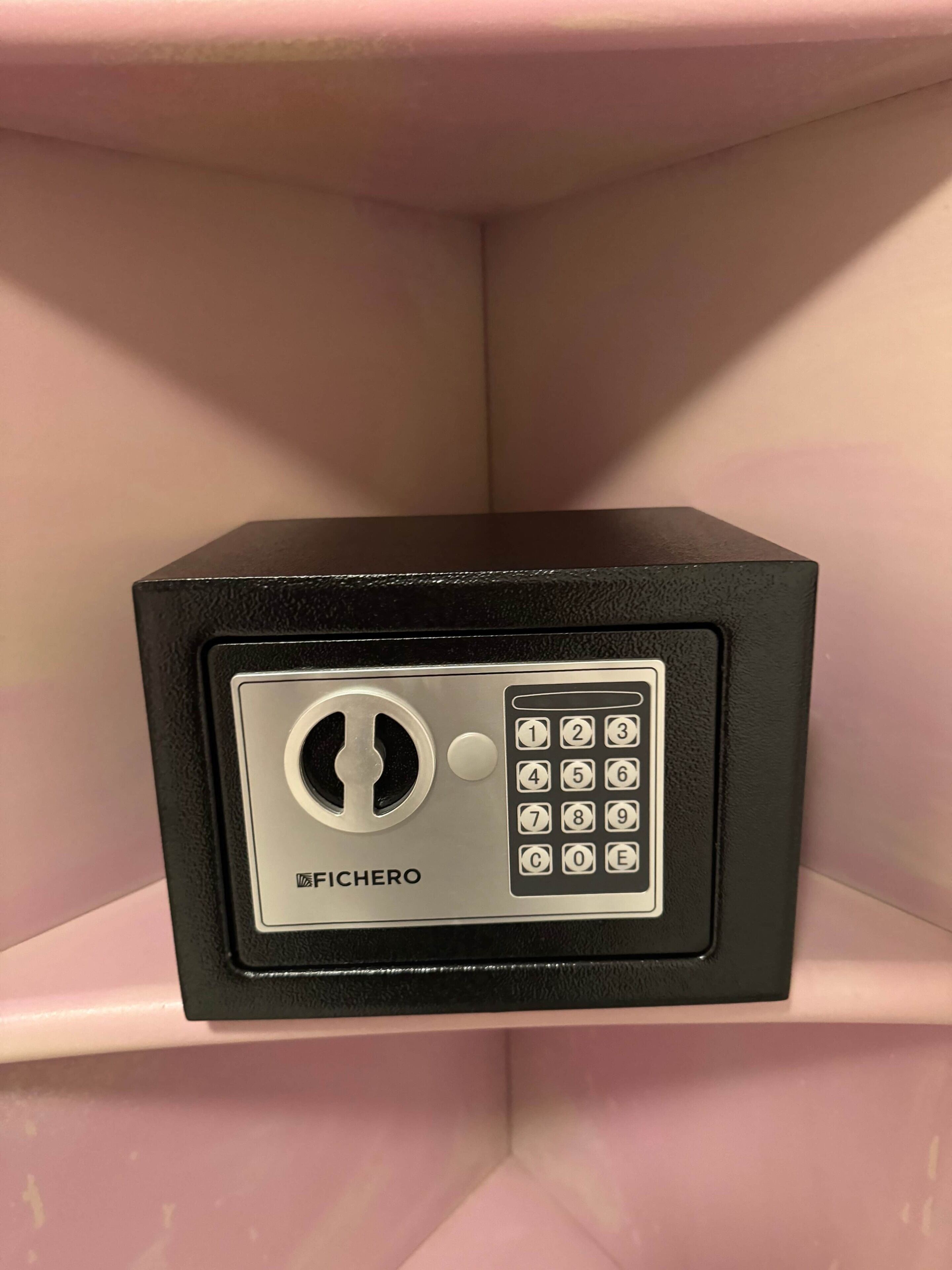 Um cofre preto com teclado e a marca 'FICHERO' numa prateleira rosa.