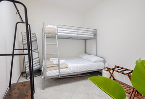 Een stapelbed met een ladder, een metalen plank, een groene stoel en een witte muur.