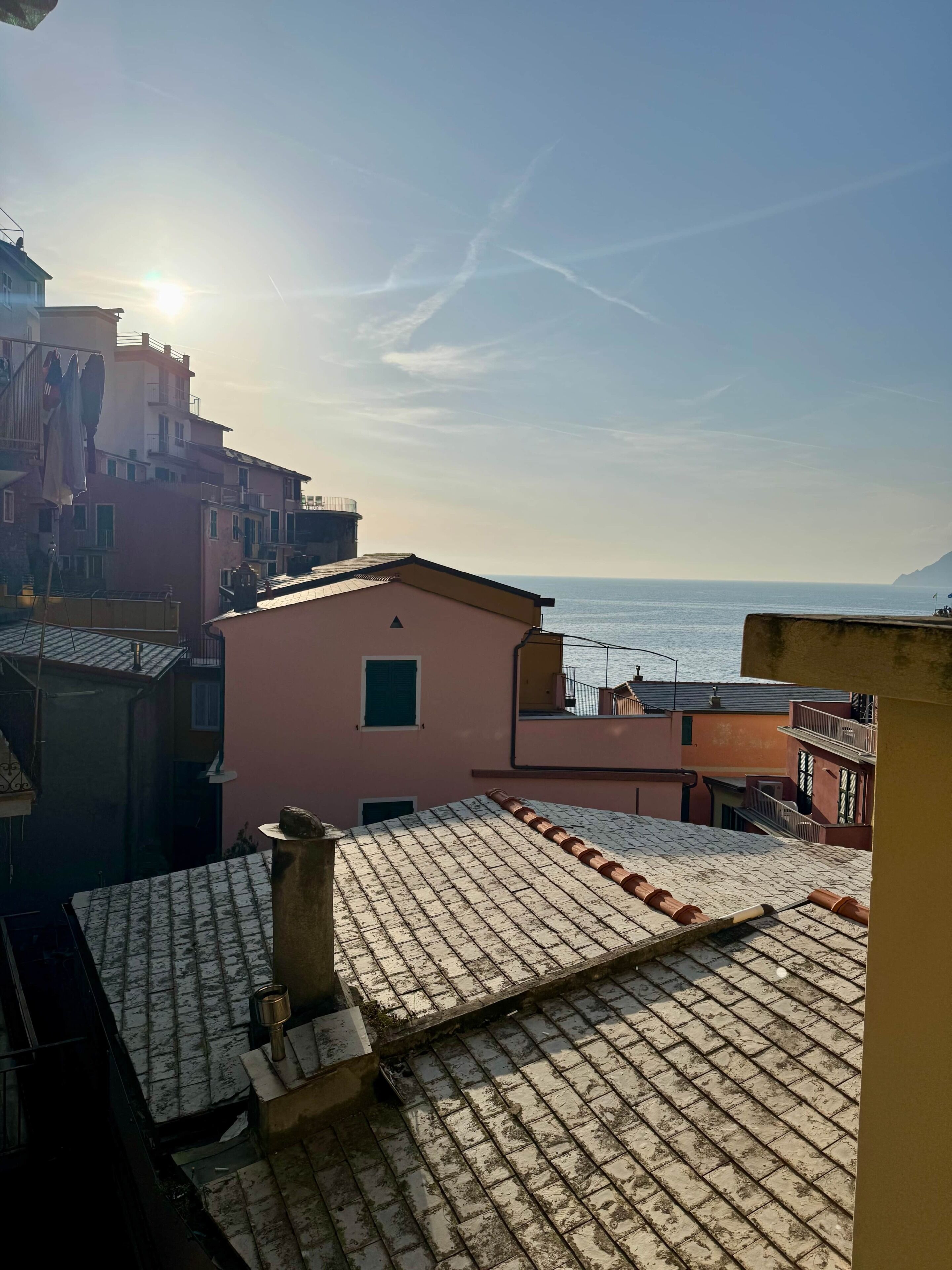A coastal residential area with terracotta roofs, a clear sky, and a view of the sea.
