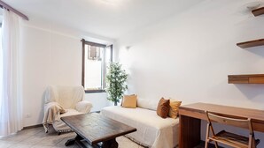 Una habitación con un sofá, una mesa de madera, una silla, una planta pequeña y una ventana con persianas.