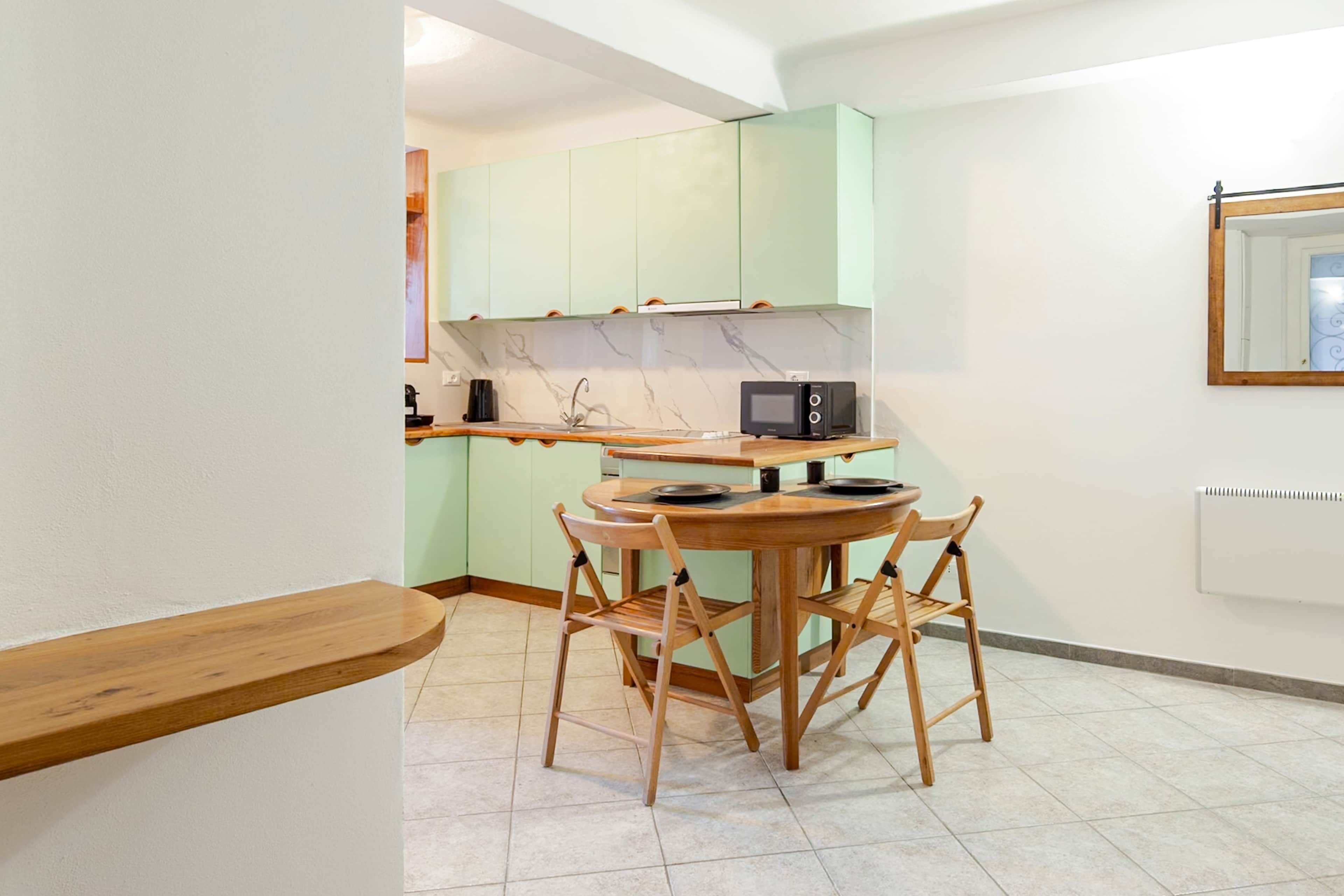 Une cuisine de taille réduite avec des meubles de couleur vert clair, une table ronde en bois et quatre chaises en bois.