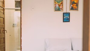 Une pièce comprenant un lit, une porte en bois, un espace douche et des tableaux accrochés au mur.