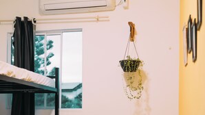 Une chambre de dortoir avec des lits superposés, une fenêtre, une plante suspendue et un climatiseur fixé au mur.