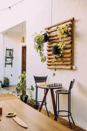 A rustic wooden wall-mounted planter with various plants, a chessboard on a table, and two wicker chairs.