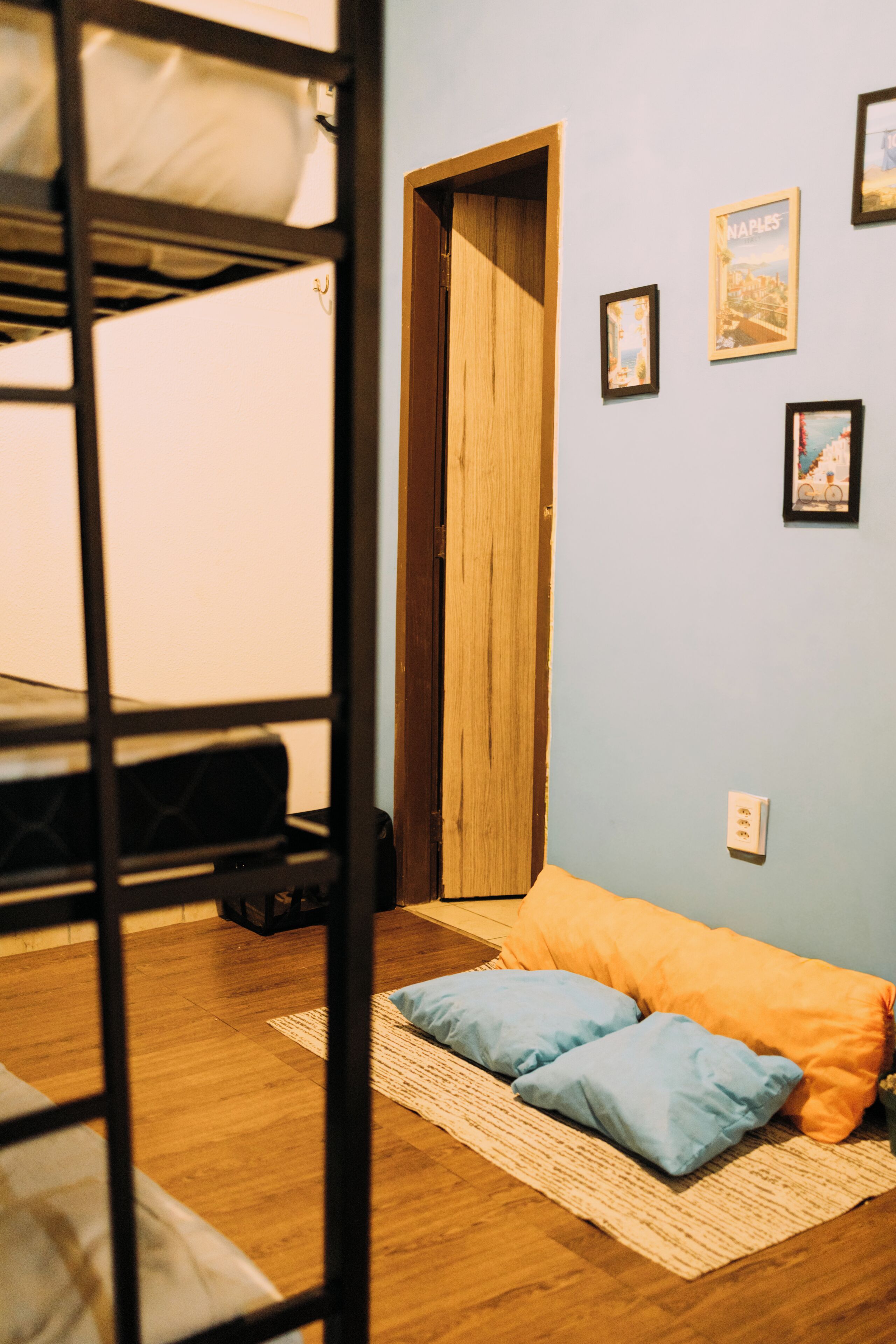 A room with a bunk bed, a door, a wall with framed pictures, a power outlet, and a rug on the floor.