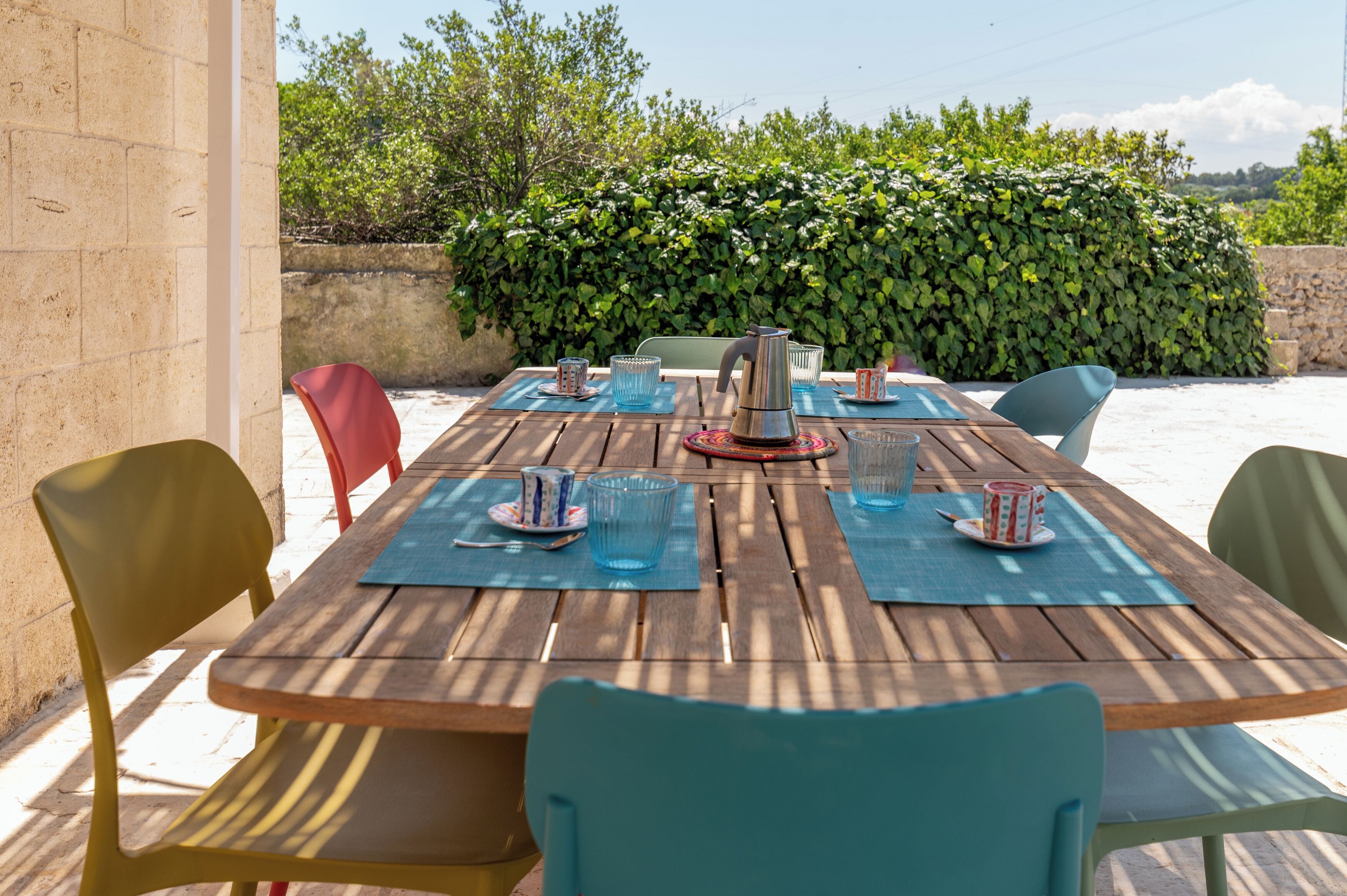 Un espace de restauration en plein air avec une table en bois, des chaises et une variété d’articles de vaisselle.