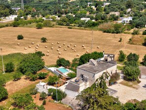 Paisaje rural con un campo de pacas de heno, un edificio con piscina y vegetación circundante.