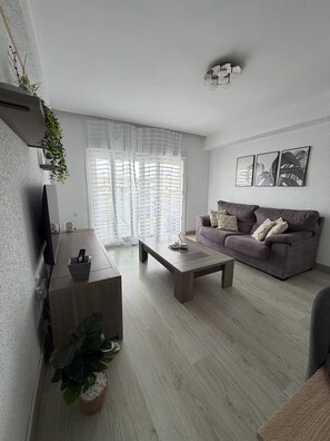 Ein modernes Wohnzimmer mit Sofa, Couchtisch, Fernseher und Pflanzen.