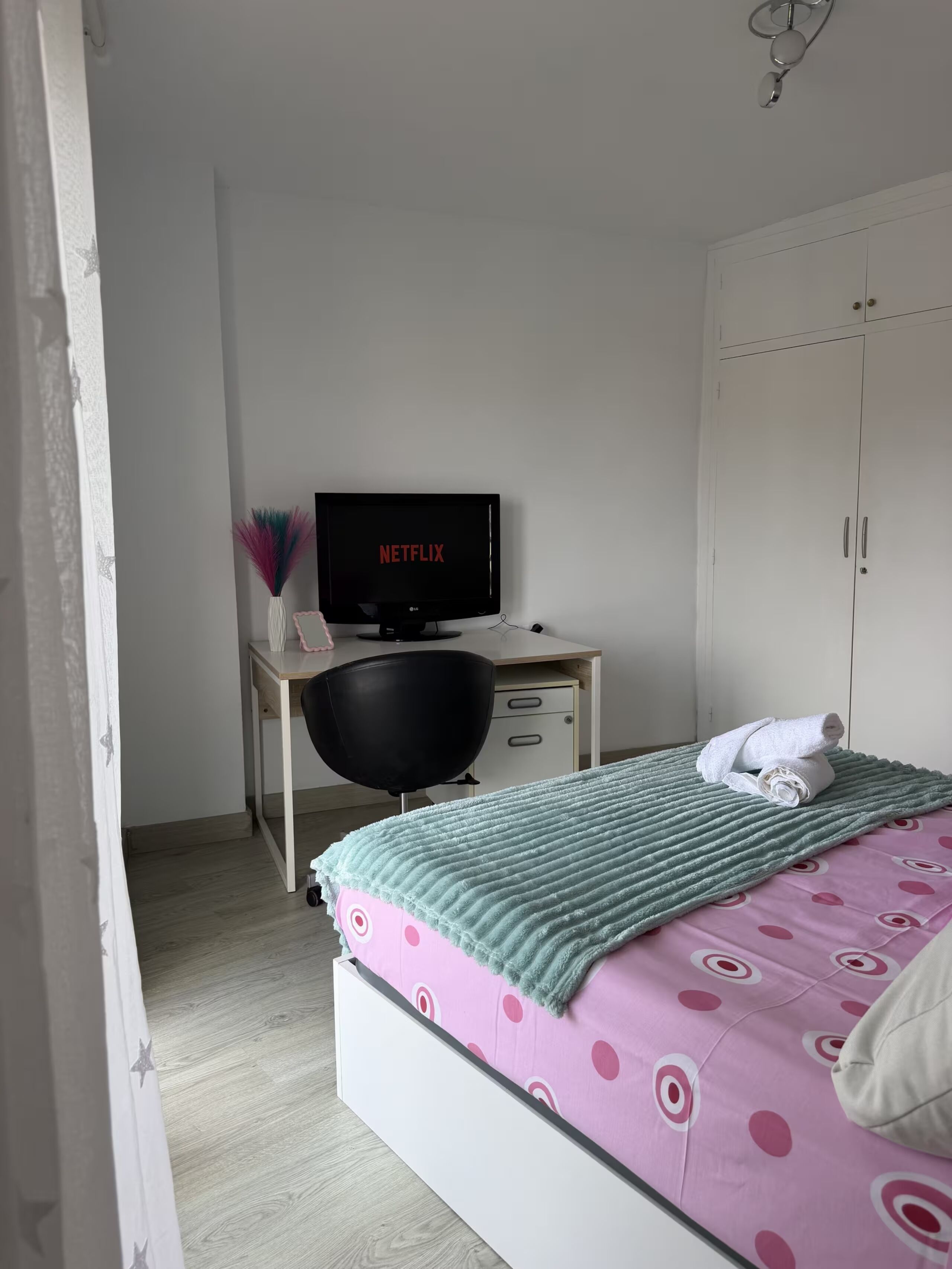 A bedroom with a bed, a desk with a computer, a wardrobe, and a window.