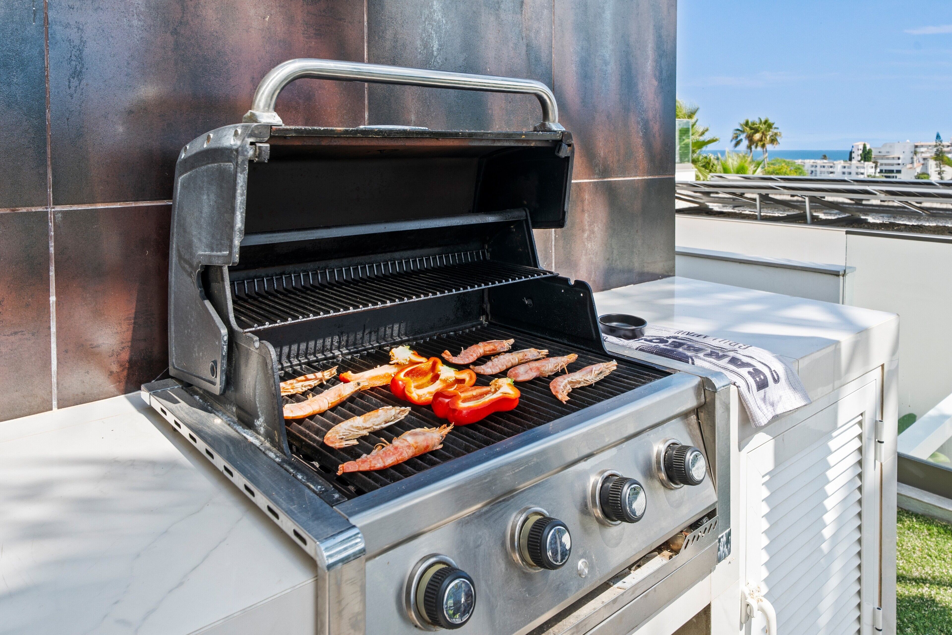 A stainless steel outdoor grill with multiple burners and a chimney, placed against a tiled wall.
