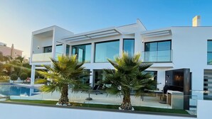 A modern two-story house with a pool, palm trees, and a clear sky. - Villa Catalina with Infinity Pool and Sea View (Armação de Pêra)
