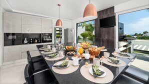 A modern kitchen with a dining area, large windows, and a view of the outdoors. - Villa Catalina with Infinity Pool and Sea View (Armação de Pêra)