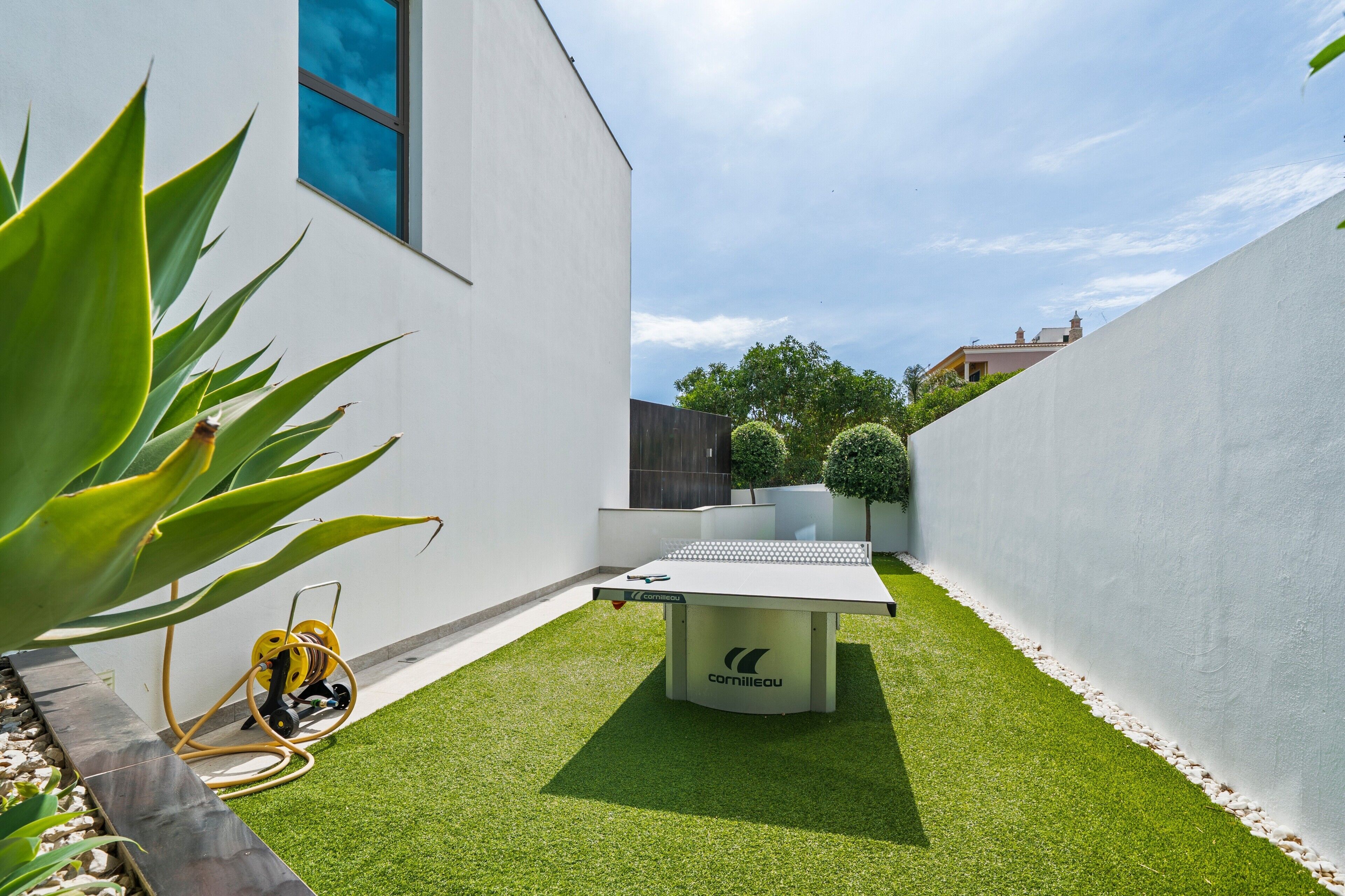 A modern outdoor area with artificial grass, a table, and a hose reel.