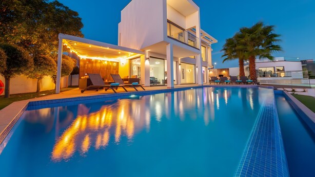 A modern two-story building with a swimming pool, outdoor seating, and a covered area with string lights. - Villa Catalina with Infinity Pool and Sea View (Armação de Pêra)