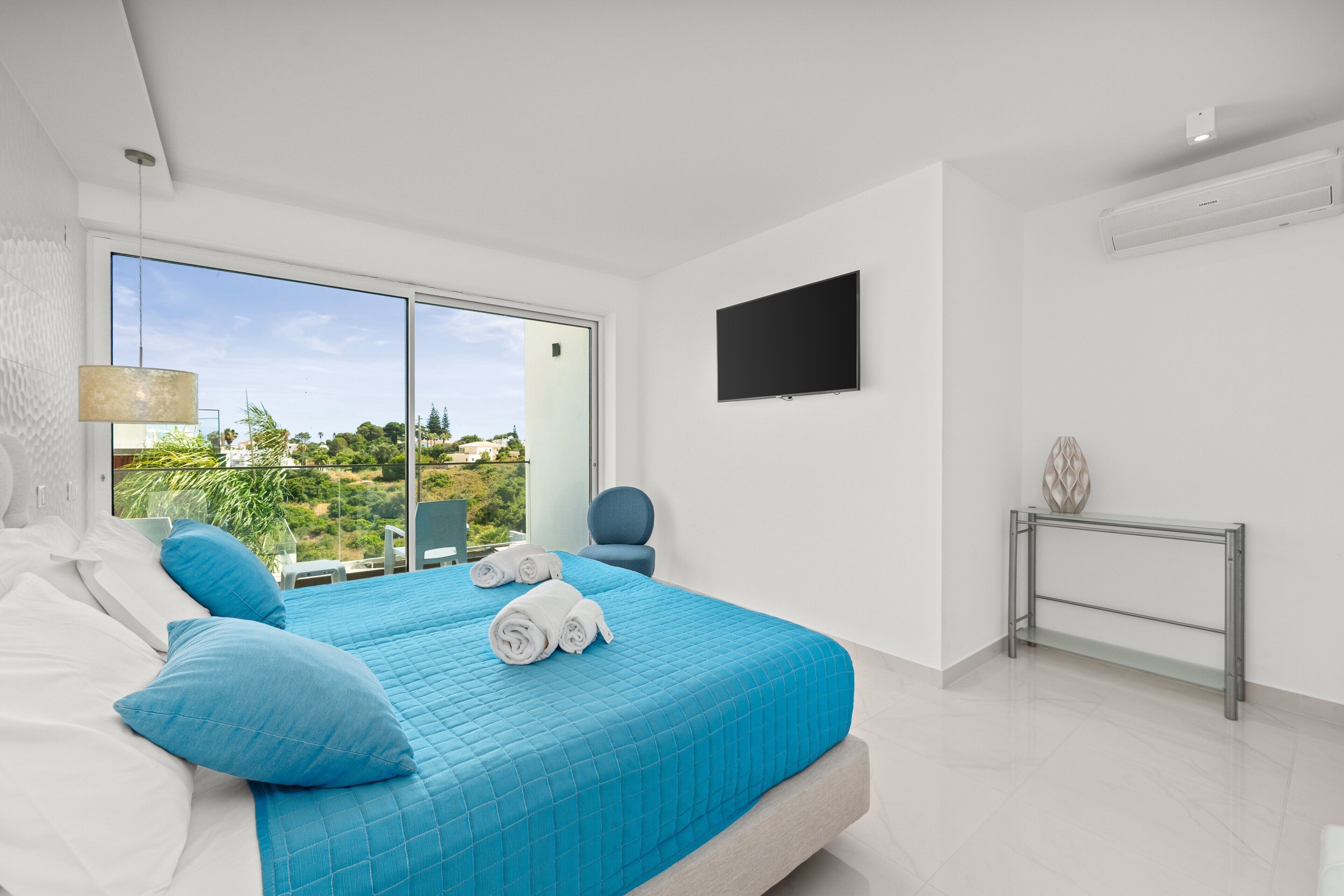 Ett modernt hotellrum med en stor säng, en TV och utsikt över omgivningarna.
