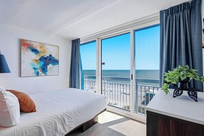 Ein Hotelzimmer mit einem Bett, einem Gemälde, einem Balkon mit Blick auf den Strand und einer Pflanze auf einem Tisch.