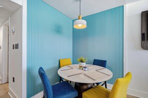 Ein Essbereich mit einem runden Tisch, blau-gelben Stühlen und einem Blumentopf.