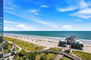A beach with a pier, a boardwalk, and a building with a blue roof. - Oceanfront Pierfection by Casanita - Lux Suite (Myrtle Beach)