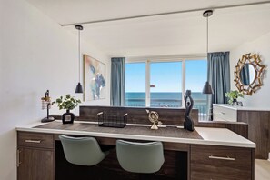 A modern kitchen with a large window, two chairs, a central island, and a view of the sea. - Oceanfront Pierfection by Casanita - Lux Suite (Myrtle Beach)