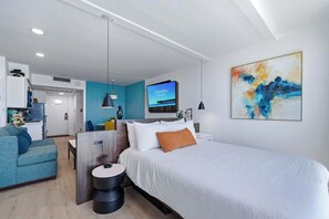 A modern hotel room with a bed, a desk, a television, and a painting. - Oceanfront Pierfection by Casanita - Lux Suite (Myrtle Beach)