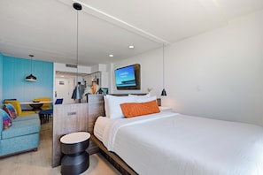 Habitación de hotel moderna con una cama grande, un televisor montado en la pared y un área de descanso con mesa y sillas.