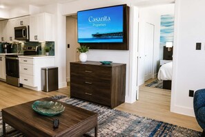 A modern kitchen with white cabinets, stainless steel appliances, and a flat-screen TV displaying 'Casamita Properties'. - High Seas by Casanita - Oceanfront Suite (Myrtle Beach)
