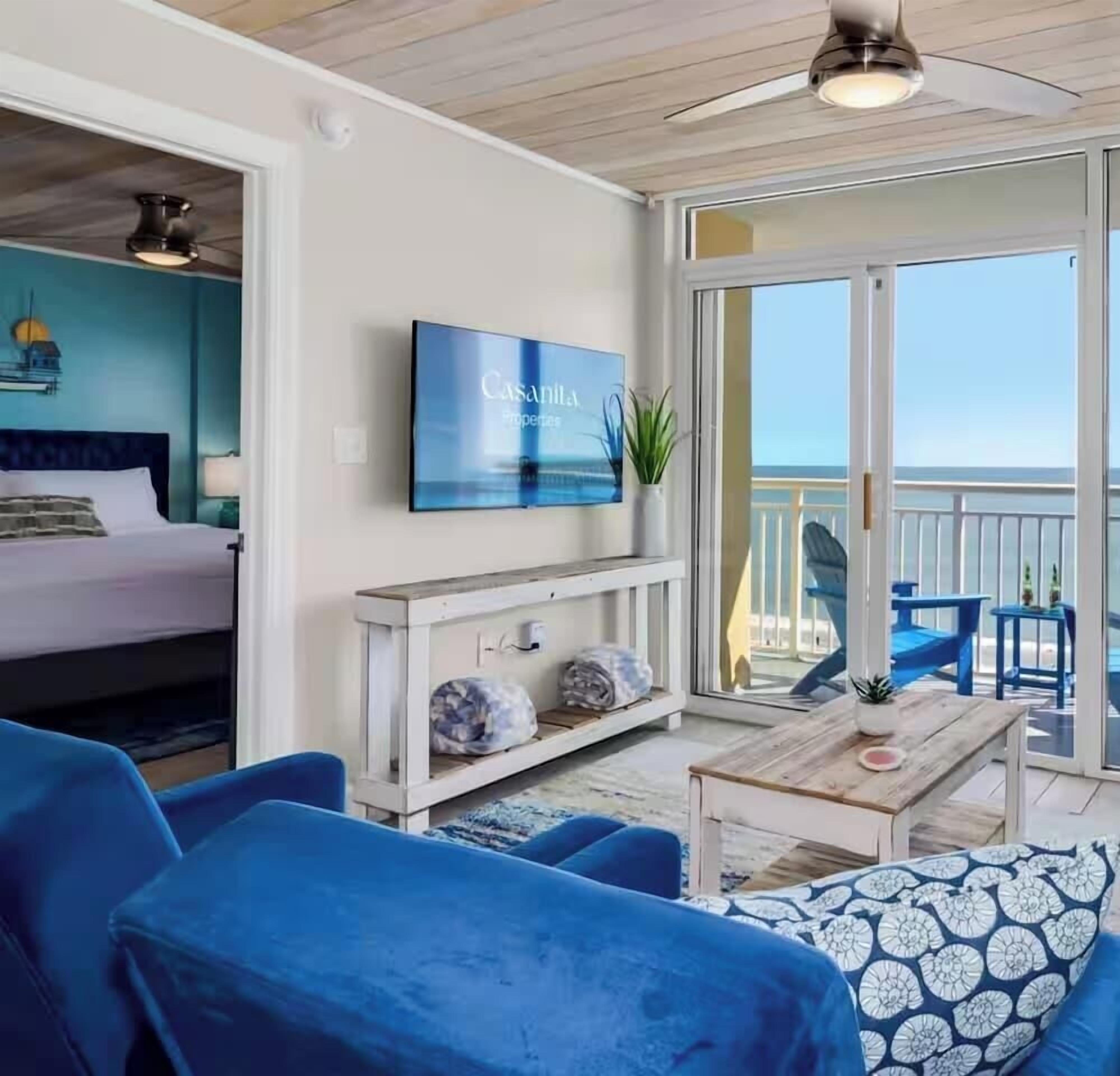 Ein Zimmer mit Bett, Fernseher, Sofa, Couchtisch und einem Balkon mit Stühlen.