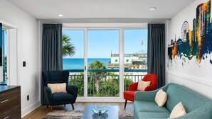 Ein Zimmer mit Meerblick, ein Balkon mit Geländer, eine Couch, ein Sessel und ein Tisch.