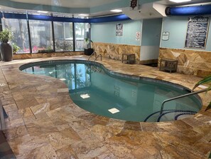 An indoor swimming pool with a stone floor, a pool ladder, and a sign indicating shallow water. - High Seas by Casanita - Oceanfront Suite (Myrtle Beach)