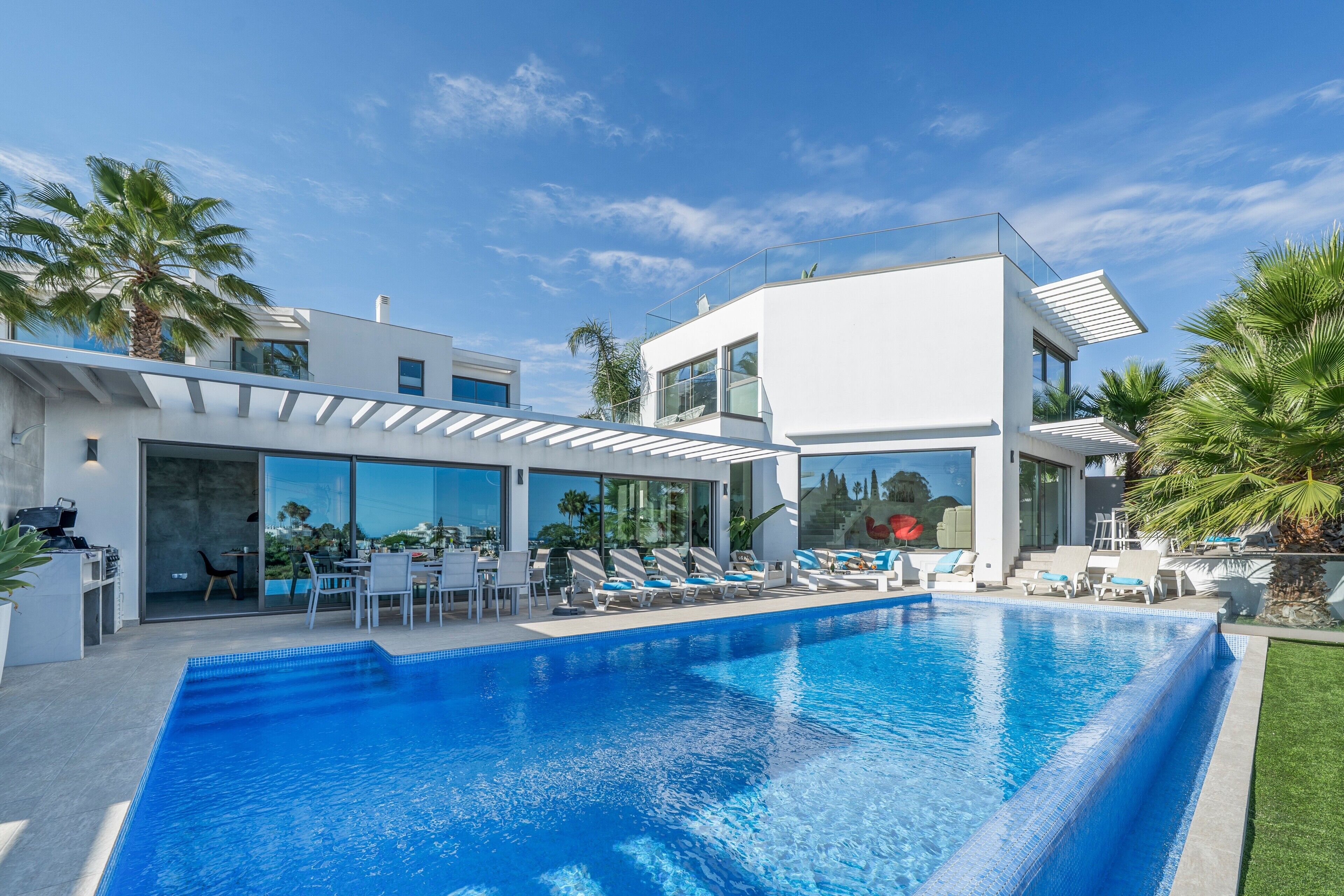 A modern house with a swimming pool, outdoor seating, and palm trees.